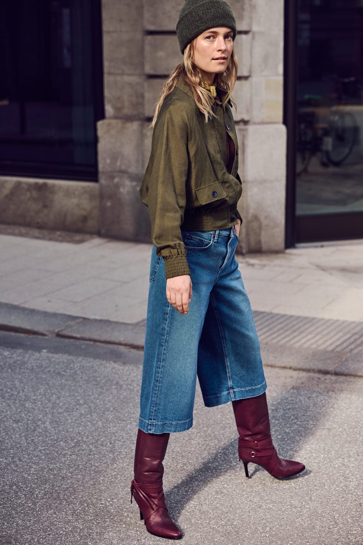Vrouw in MAC jeans met wijde pijpen en bordeauxrode laarzen die een stadsstraat oversteekt